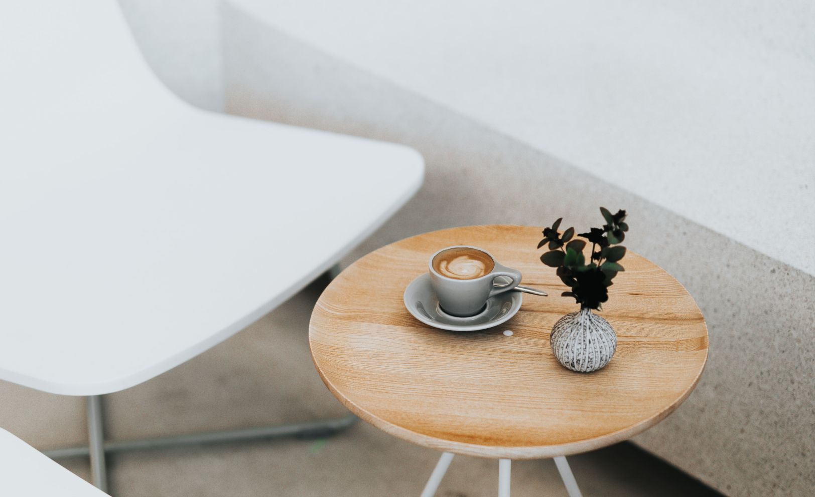 A white chair beside a wooden side table with a cup of coffee and a small plant